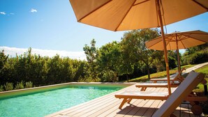 Una terraza de madera con piscina, sillas de descanso y sombrillas.