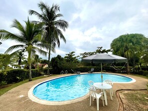 A swimming pool with a white table and chairs, surrounded by palm trees and a covered umbrella. - San Lorenzo (Melgar)
