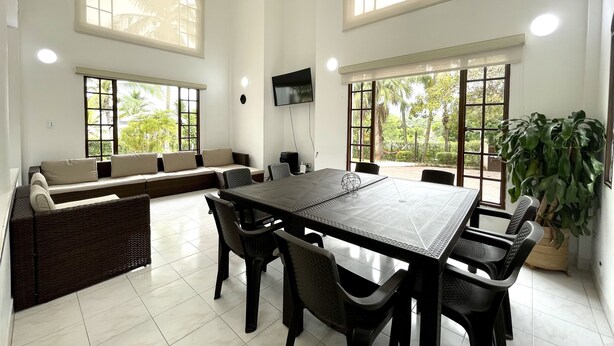 Amplia habitación con una gran mesa de comedor, asientos cómodos y ventanas grandes con vistas a la vegetación.