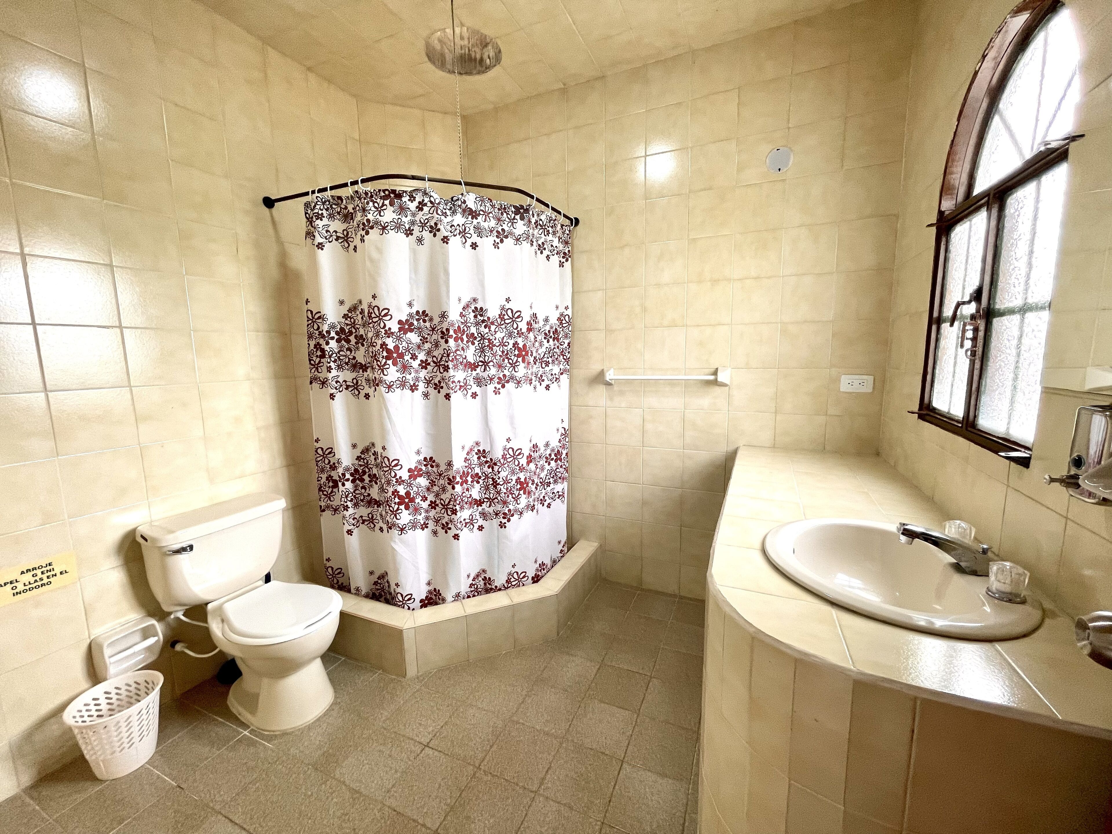 Une salle de bain avec des toilettes, un rideau de douche, un lavabo et une fenêtre.