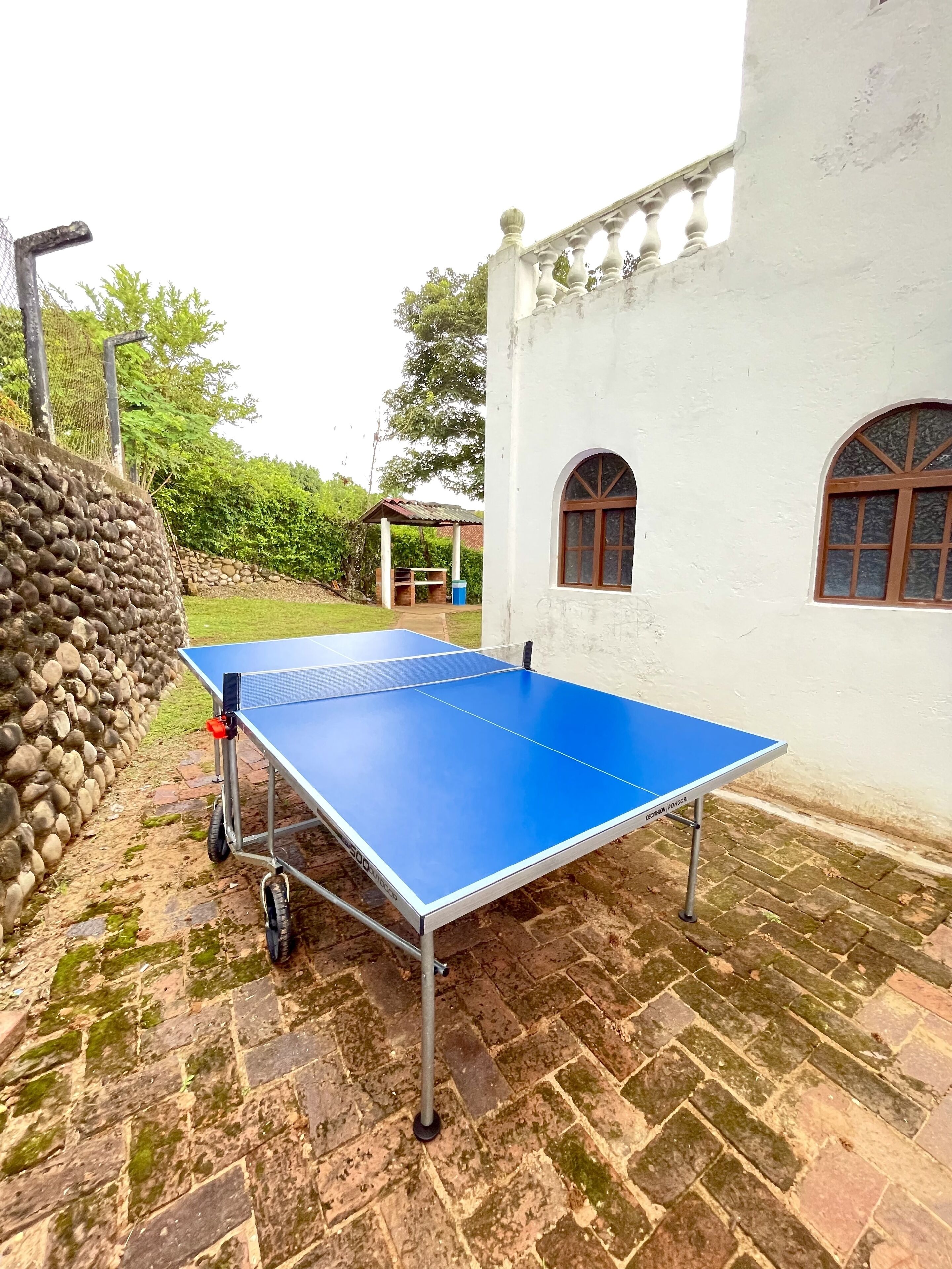 A ping pong table set up outdoors on a brick patio, adjacent to a white building with arched windows.