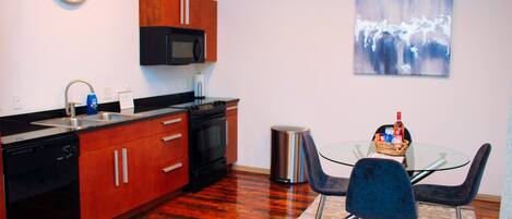 A modern kitchen with wooden cabinets, a microwave, and a dishwasher. There's a dining area with a glass table and two chairs.