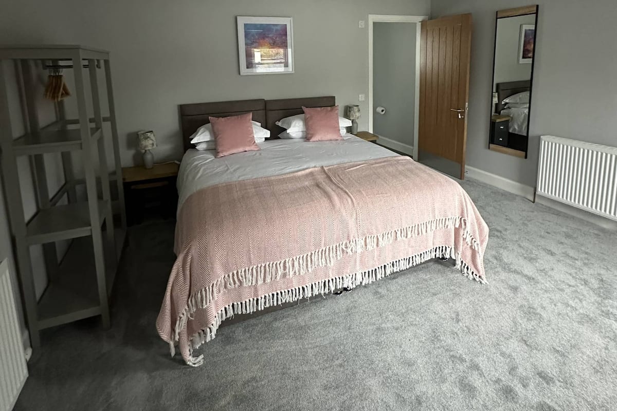Un dormitorio con cama, armario de madera, mesita de noche, un cuadro enmarco y un radiador.