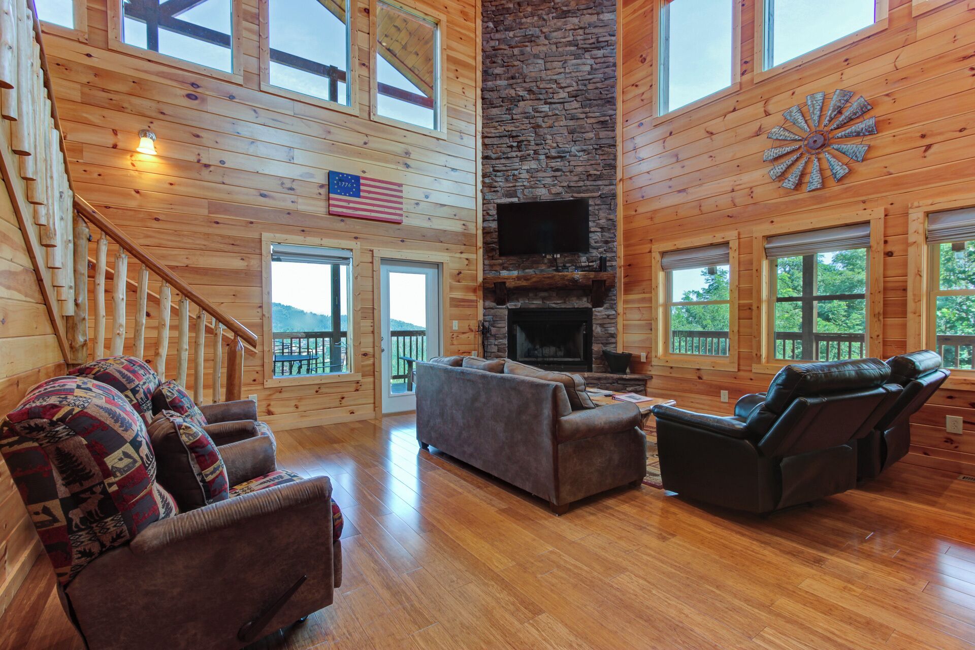 A spacious living room with a stone fireplace, wooden walls, and large windows offering a view of the outdoors.