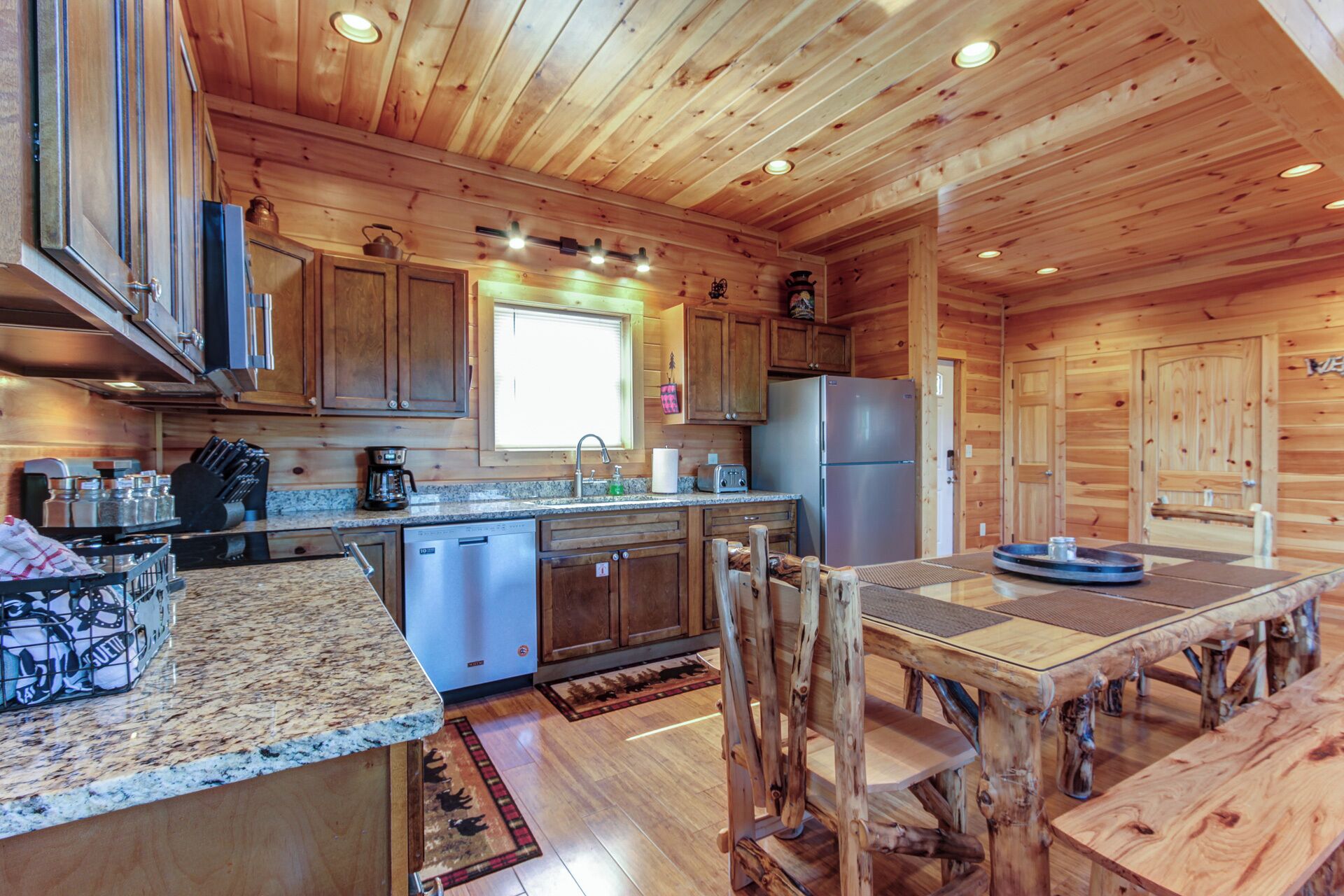 A wooden cabin-style kitchen with a granite countertop, stainless steel appliances, and a rustic dining table.