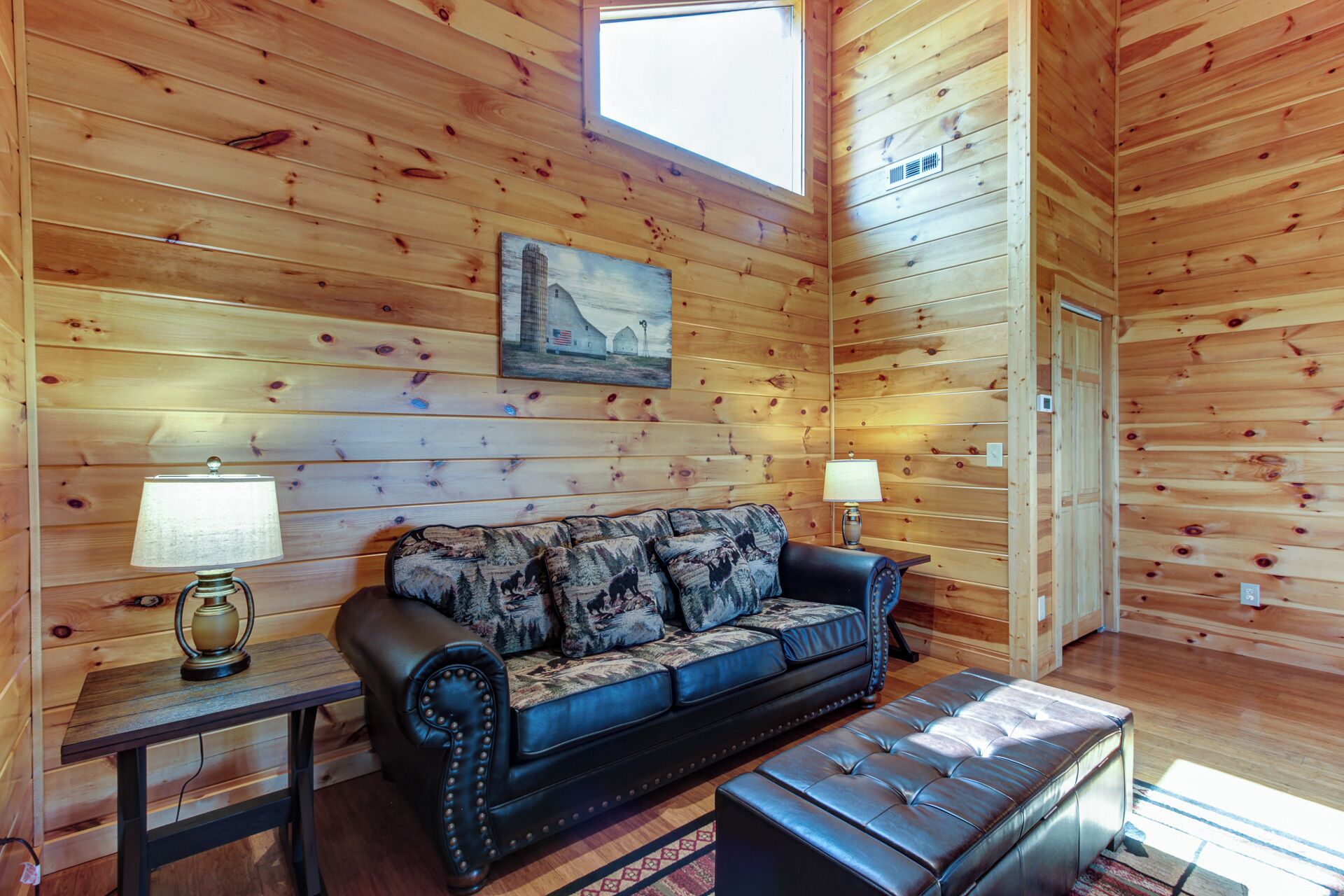 Interior acogedor de una cabaña con pared de madera, un sofá, una mesa con lámpara y una ventana.