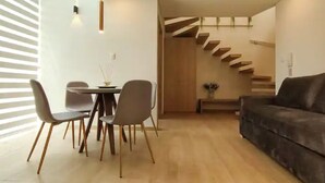 Un salon moderne avec un canapé en cuir marron foncé, une table à manger avec quatre chaises et un escalier avec des marches en bois.