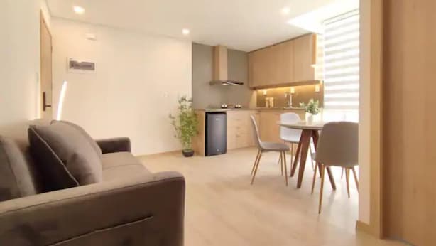 Un salon moderne avec un canapé, un coin repas comprenant une table et des chaises, et une cuisine équipée de placards et d’une cuisinière.