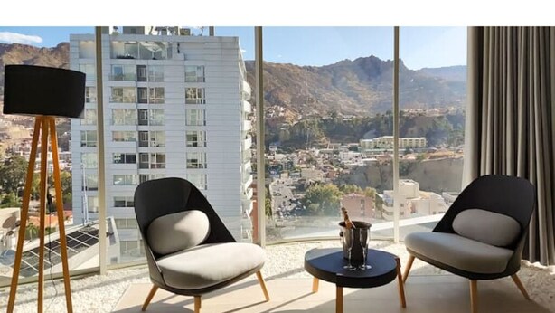 Een moderne kamer met twee stoelen, een klein tafeltje en een groot raam met uitzicht op de stad.
