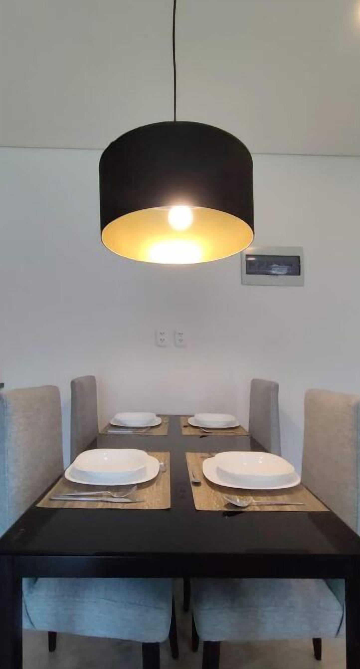 Un comedor con una mesa negra, cuatro platos blancos y una lámpara colgante negra.