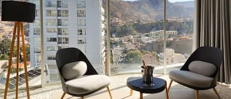 A modern room with two chairs, a small table, and a large window offering a city view.