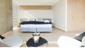 Een moderne slaapkamer met een bed, een nachtkastje met lamp en uitzicht op buiten.