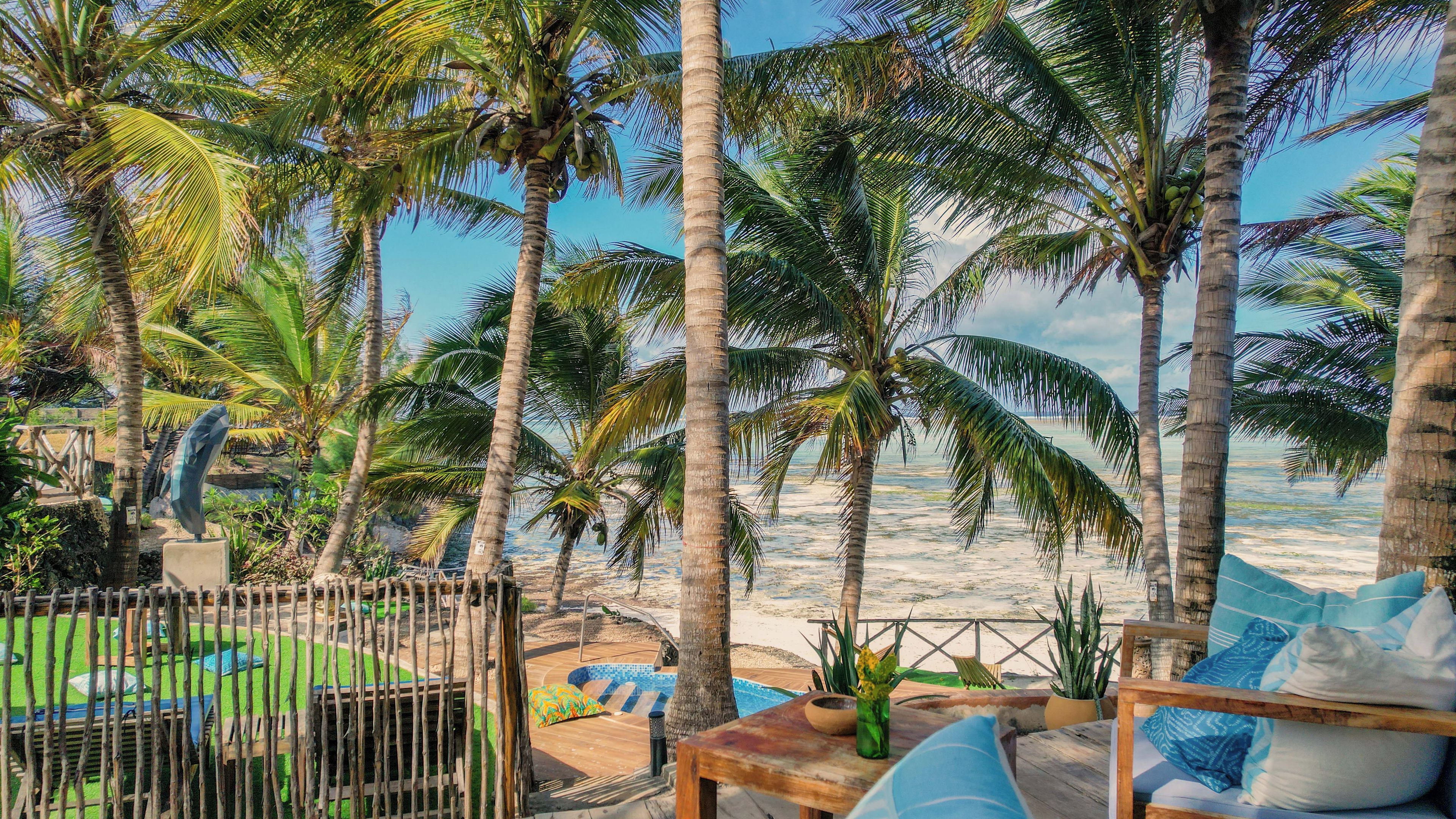 A beachside patio with a wooden table, chairs, and a view of the ocean.