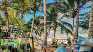 A beachside patio with a wooden table, chairs, and a view of the ocean. - Ocean View Private Beach Villa 2 Pools 7 Ensuite Bedrooms Fully Staffed (Makunduchi)