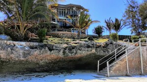 A coastal hotel with a rocky cliff, palm trees, and a staircase leading to a building. - Private Beach Villa & 2 Pools, Sleeps Upto 22 (Makunduchi)
