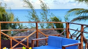 A wooden deck with blue cushioned seating and a table, overlooking a beach with palm trees and the ocean. - Private Beach Villa & 2 Pools, Sleeps Upto 22 (Makunduchi)