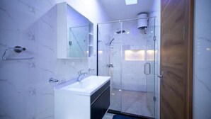 Une salle de bain moderne avec une douche à l’italienne en verre, un lavabo blanc et un grand miroir.
