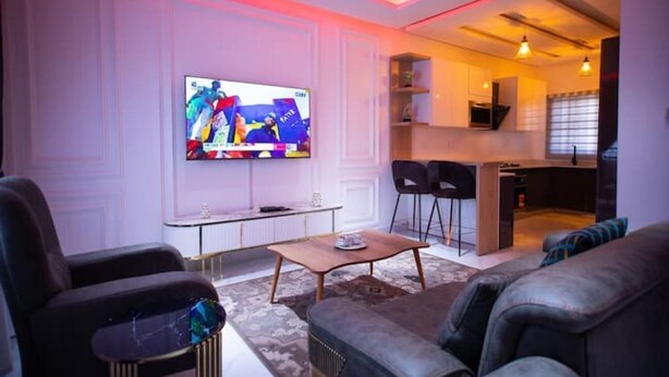 Un salon moderne avec un téléviseur à écran plat, un canapé, une table basse et un coin cuisine à l’arrière-plan.