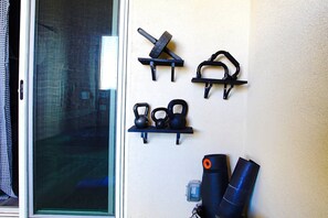 A wall-mounted rack holding kettlebells, a kettlebell, and a kettlebell handle. - Beach Breeze Bungalow King (Lawndale)