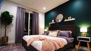 Une chambre à coucher moderne avec un grand lit, une table de chevet avec une lampe, une plante en pot et une vue sur l’extérieur grâce à une porte coulissante.