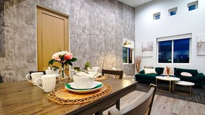 Un espace repas moderne avec une table en bois dressée pour un repas, un canapé vert et une vue sur la ville par la fenêtre.