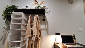 Une chambre moderne avec un porte-manteau mural où sont suspendues plusieurs peignoirs, un ordinateur portable posé sur un bureau et une petite plante en pot.