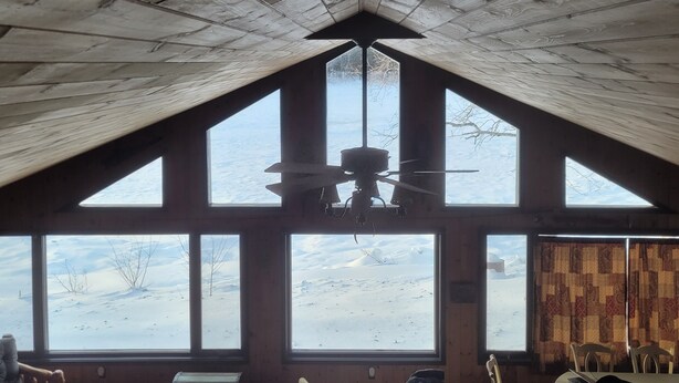 A high-ceilinged room with a sloped roof, large windows, and a ceiling fan. - Tranquil Riverside Lodge (Wade)