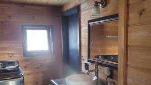A wooden cabin interior with a sink, mirror, and a window. - Tranquil Riverside Lodge (Wade)