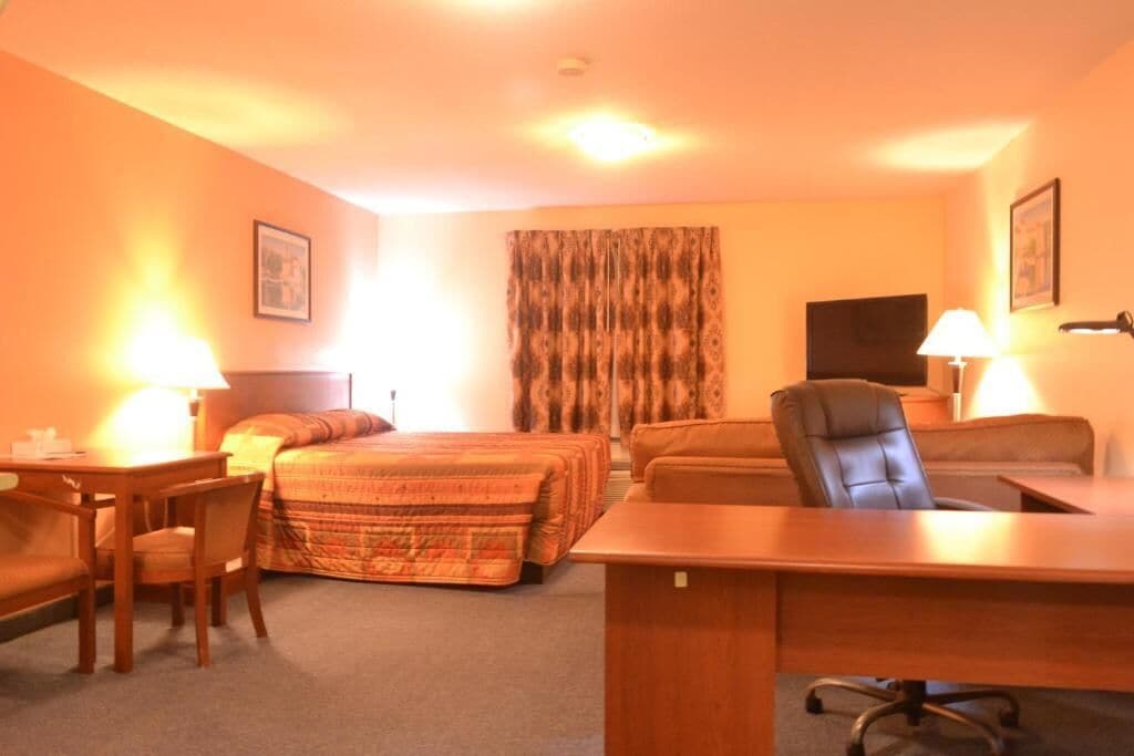A hotel room with a bed, a desk, a chair, a television, and a lamp.