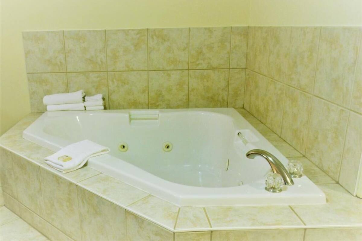 Eine große, rechteckige Badewanne mit einem Wasserhahn und einer Bedienkonsole, eingebettet in eine Ecke mit beigen Fliesen.