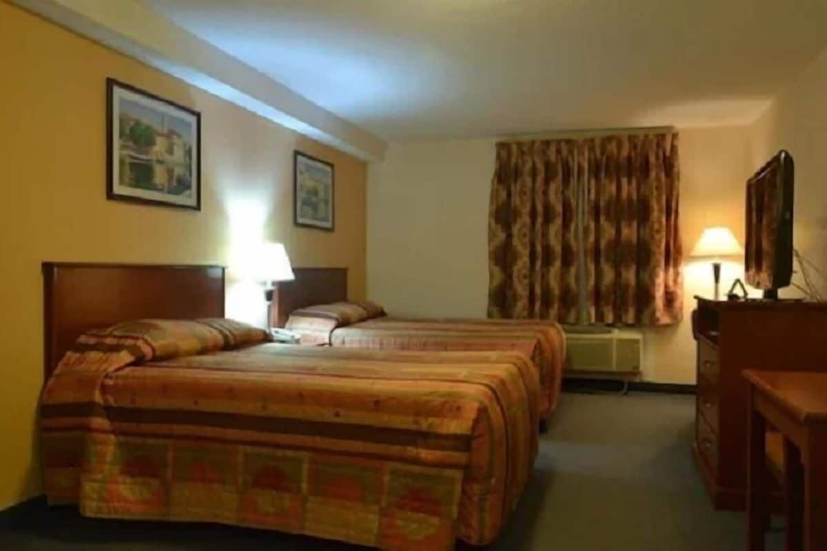 Ein Hotelzimmer mit zwei Betten, einem Schreibtisch, einem Stuhl, einer Lampe und einem Bild an der Wand.