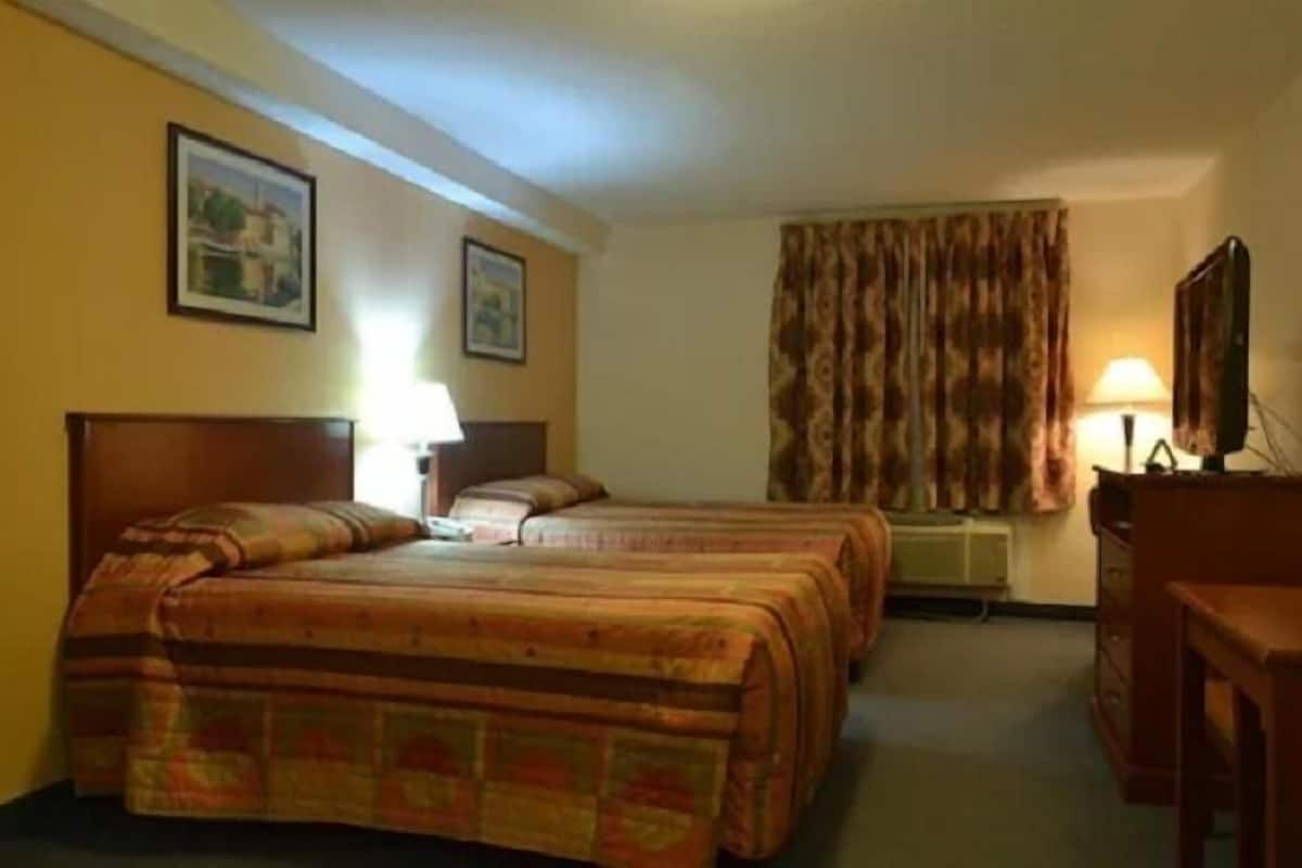 Ein Hotelzimmer mit zwei Betten, einem Schreibtisch, einem Stuhl, einer Lampe und einem Fenster mit Vorhängen.