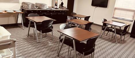 A conference room with tables and chairs, a projector, and a flat-screen TV on the wall.