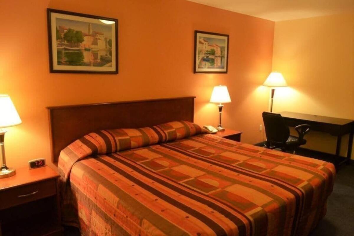 Ein Hotelzimmer mit einem Bett, zwei Nachttischlampen, einem Schreibtisch mit Stuhl und zwei gerahmten Bildern an der Wand.