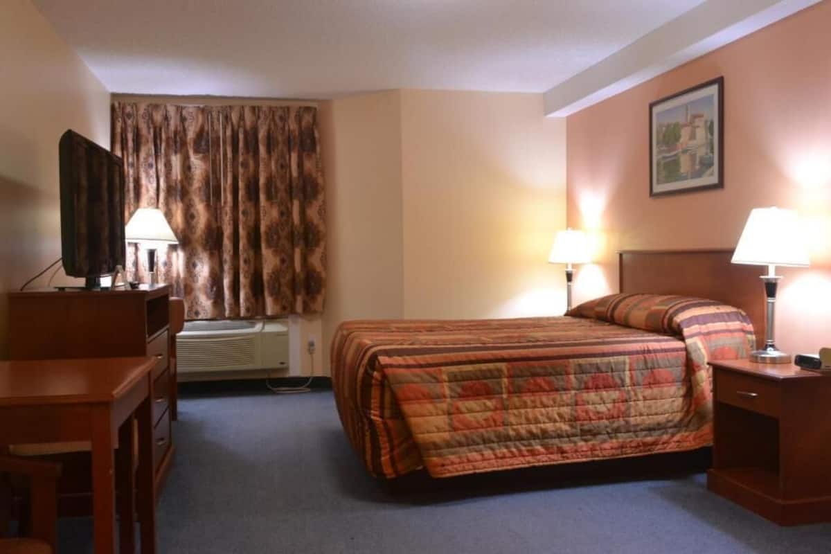 Ein Hotelzimmer mit einem Bett, einem Schreibtisch, einem Sessel, einem Fernseher und zwei Lampen.
