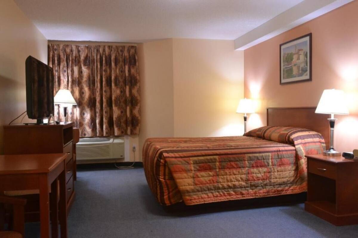 Ein Hotelzimmer mit einem Bett, einem Schreibtisch, einem Stuhl, einem Fernseher und einem Bild an der Wand.