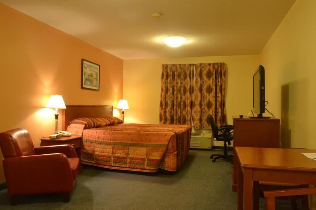 A hotel room with a bed, two chairs, a desk, a television, and a window with curtains.