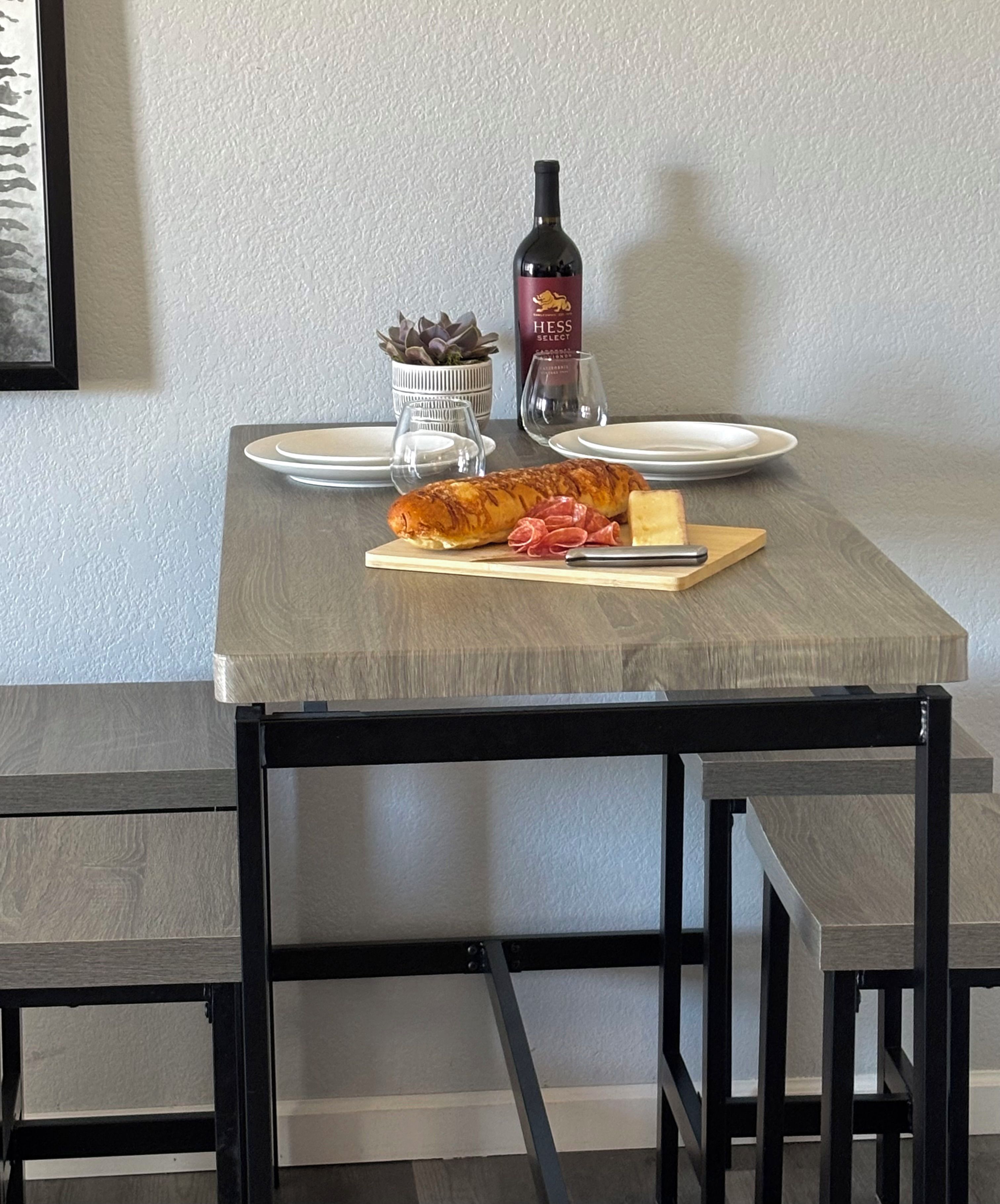 Une table à manger avec des assiettes, une bouteille de vin, un verre, un pain et une planche à découper avec de la viande tranchée.