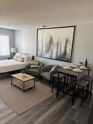 Un dormitorio moderno con cama, sofá, mesa de centro y zona de comedor con mesa y sillas.