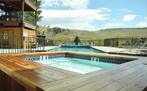 Et poolområde med træterrasse, jacuzzi og udsigt til et bakket landskab.