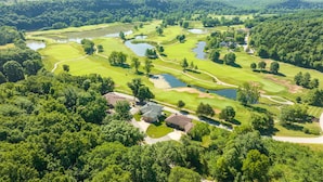 An aerial view of a golf course with multiple ponds, surrounded by dense forest and residential buildings. - Overlooking 9th Green at Osage National Golf Resort (Lake Ozark)