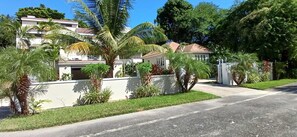 Una calle residencial con casas, palmeras y una entrada protegida por un portón.