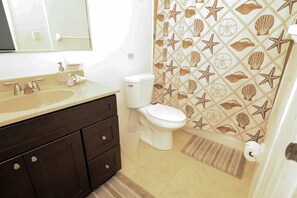 A bathroom with a beige sink, dark wooden vanity, white toilet, and a shower curtain with a starfish and shell pattern.