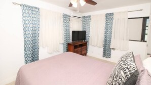 Une chambre à coucher avec un lit, un ventilateur de plafond, une télévision et des rideaux à motifs.