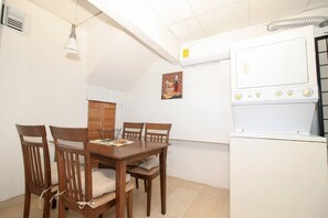 A compact kitchen with a dining table and chairs, an air conditioning unit, and a white refrigerator.