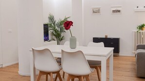 Un comedor moderno con una mesa y sillas blancas, un jarrón con una flor roja, y un mueble negro al fondo.