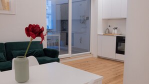Un espacio moderno con una mesa blanca, un sofá verde y un florero con una flor roja.