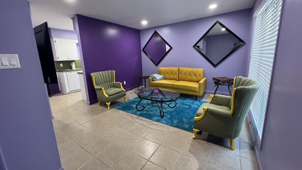 A living room with a yellow sofa, green armchairs, and a blue rug. - Retro Centrally Located Duplex! (Fort Smith)