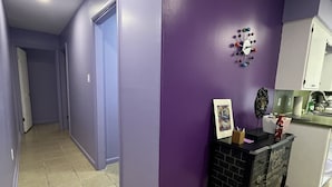 A hallway with purple walls and a tiled floor leading to a kitchen area. - Retro Centrally Located Duplex! (Fort Smith)