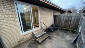A residential backyard with a brick house, a sliding glass door, a concrete patio, and a wooden fence. - Retro Centrally Located Duplex! (Fort Smith)